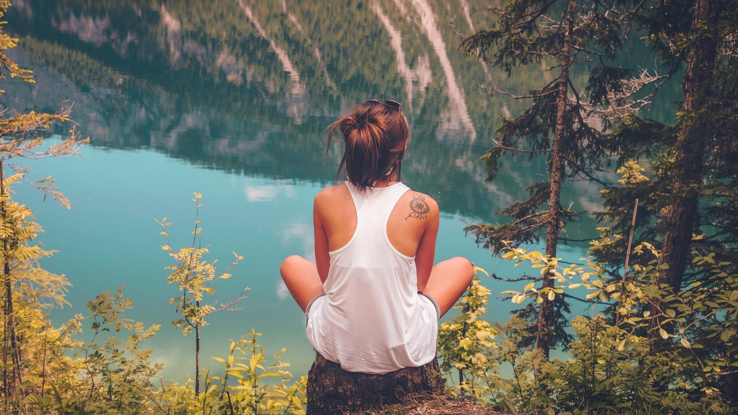 mujer sentada frente al lago en montaña