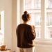 Mujer de espaldas mirando por la ventana con una taza de café en la mano